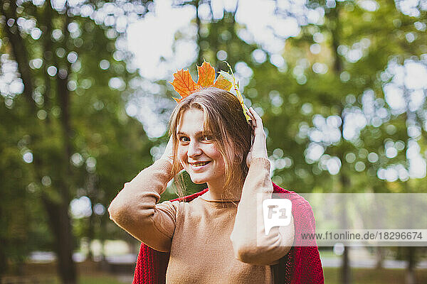 Smiling woman holding maple leaves on head at park