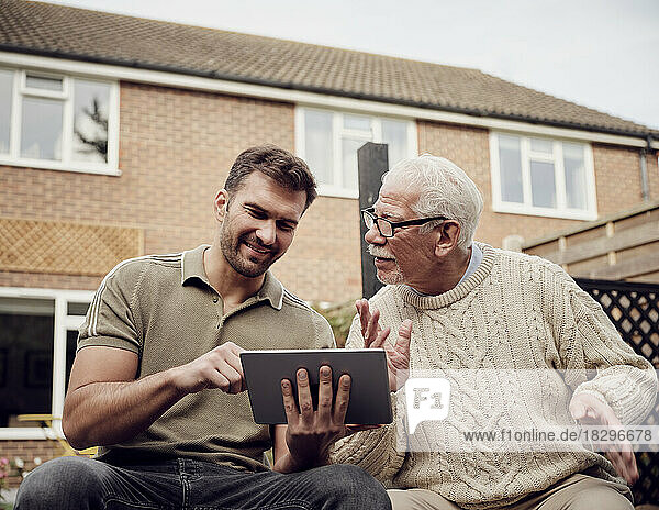 Father and son sitting in garden using digital tablet