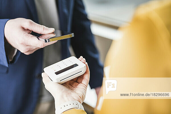 Young businessman paying through smart phone on card reader machine