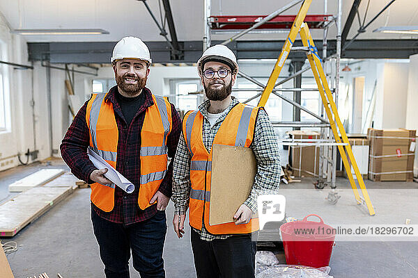Lächelnder junger Ingenieur steht mit Kollegen auf der Baustelle