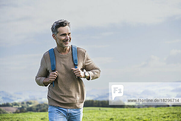 Smiling mature man with backpack walking in front of sky