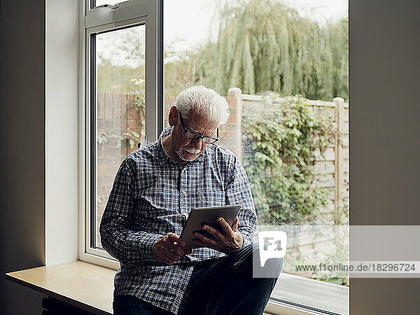 Älterer Mann am Fenster zu Hause mit digitalem Tablet