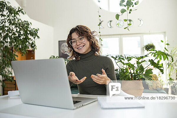 Happy young woman gesturing on video call through laptop at home