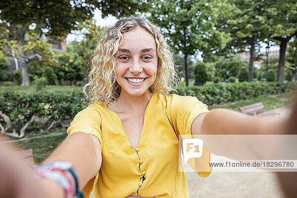 Glückliche junge Frau mit blonden Haaren macht ein Selfie im Park