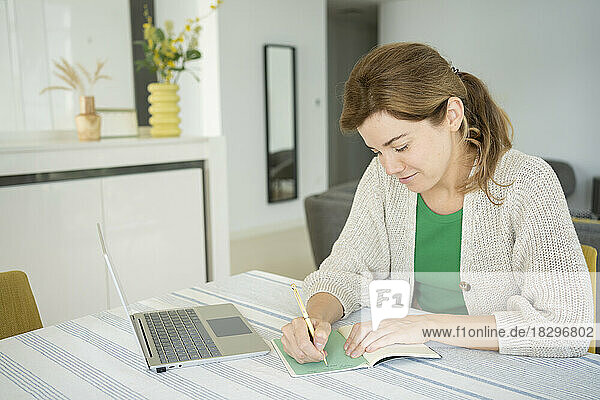 Freelancer woman making notes in note pad on desk at home office