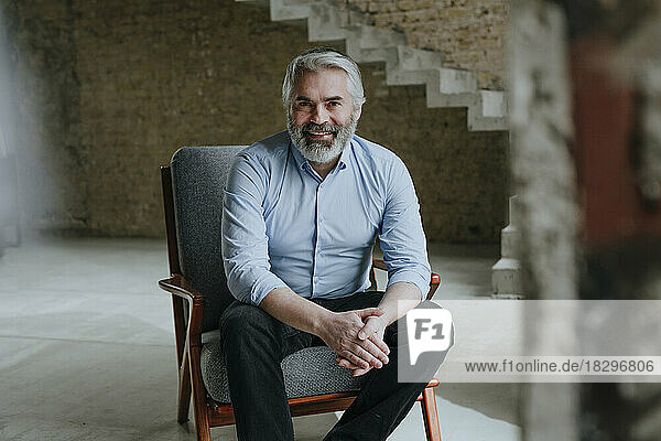 Happy mature businessman sitting in chair at under construction site