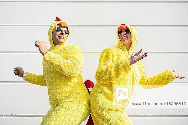 Glückliche Frau und Mann in gelben Hühnerkostümen  die Spaß vor der Wand haben