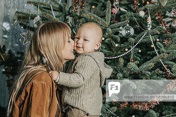 Happy mother embracing baby boy in front of Christmas tree