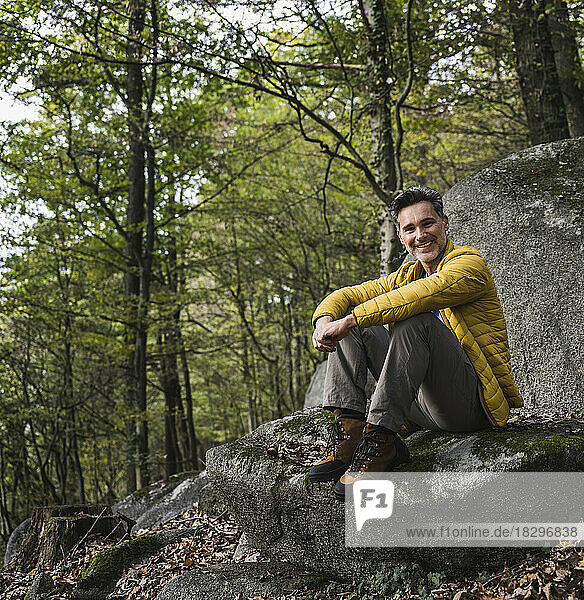 Happy mature man sitting on rock in forest