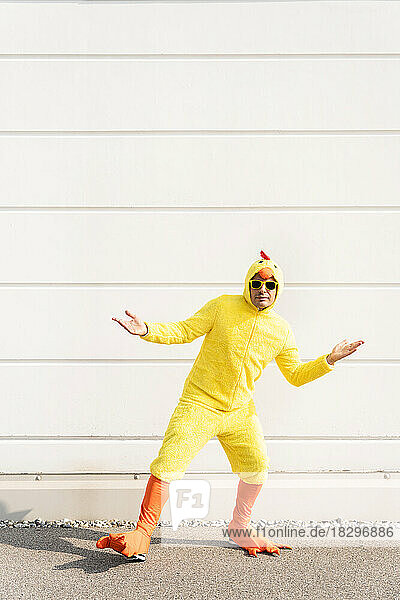 Man wearing yellow chicken costume gesturing in front of wall