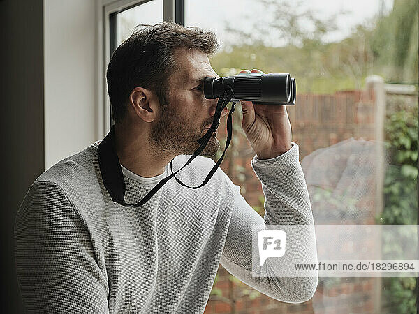 Man looking out of the window at home with binoculars
