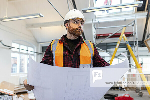 Young engineer standing with blueprint at construction site