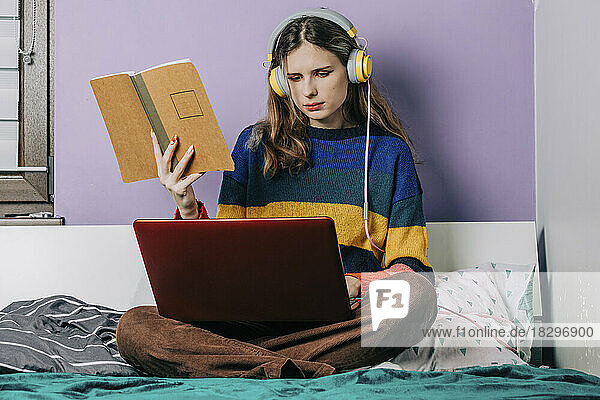 Girl using laptop doing homework sitting on bed in front of wall