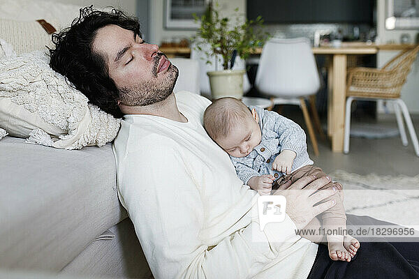 Father and baby boy sleeping together in living room at home