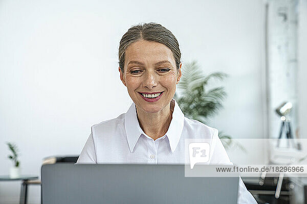 Glückliche reife Geschäftsfrau  die im Büro einen Laptop benutzt