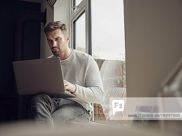 Man by the window at home using laptop