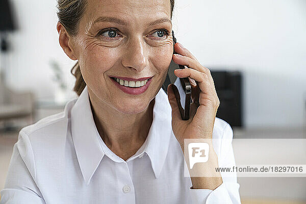Glückliche reife Geschäftsfrau  die im Büro über ihr Smartphone spricht