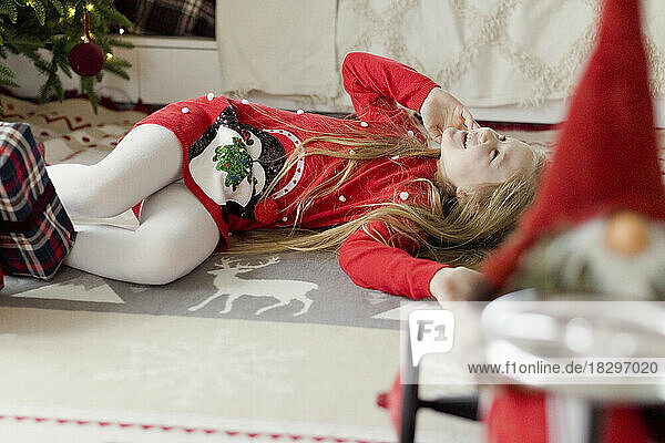 Cheerful blond girl playing and enjoying by lying on rug at home