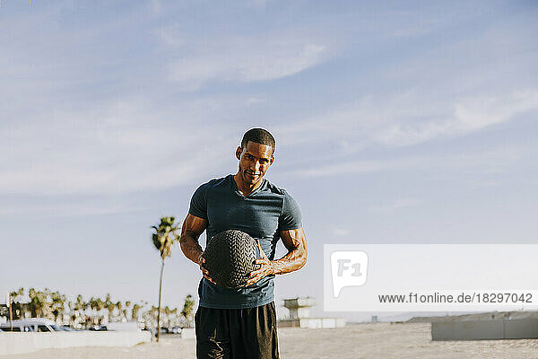 Smiling sportsman standing with ball on sunny day