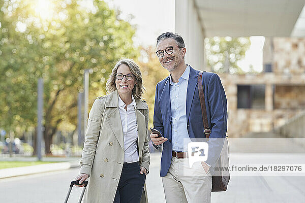 Happy mature businessman with mobile phone by colleague on footpath