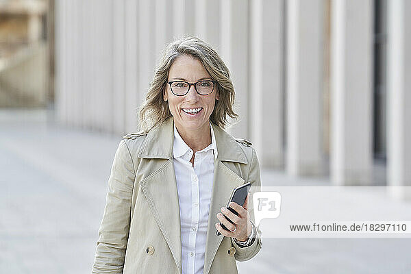 Happy mature businesswoman wearing eyeglasses standing with mobile phone