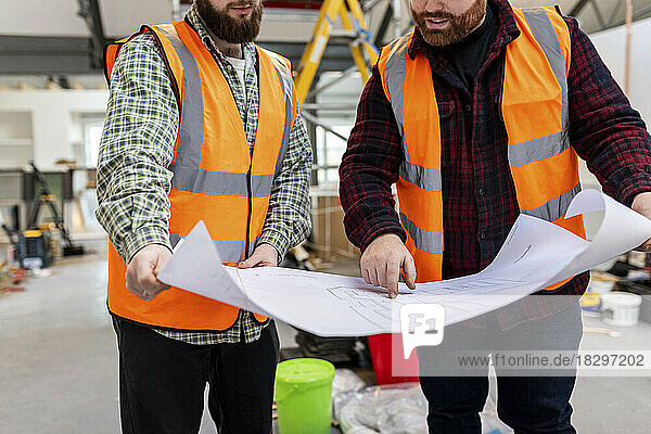 Engineers in reflective workwear discussing over blueprint at construction site