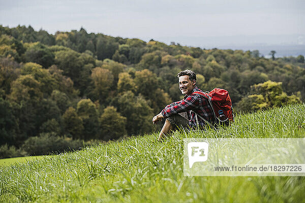 Lächelnder Mann mit Rucksack sitzt auf Gras