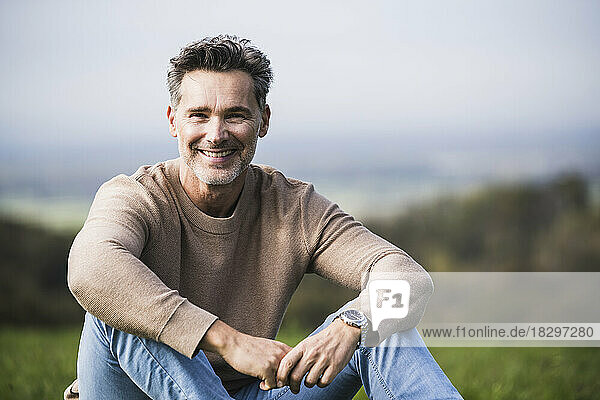 Happy mature man sitting in front of sky