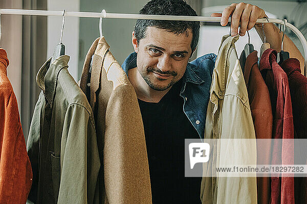 Smiling man standing behind clothes rack