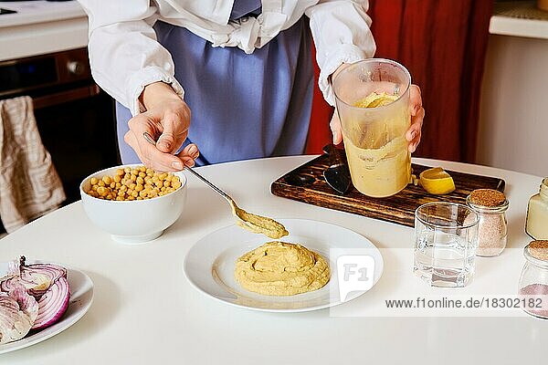 Unbekannte Frau legt Hummus auf einen Teller. Handgemachte frische Lebensmittel