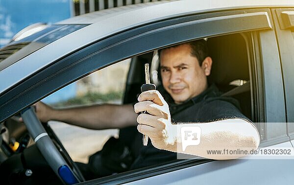 Fahrer in seinem Auto zeigt die Schlüssel aus dem Fenster. Glücklicher Mann zeigt seine neuen Autoschlüssel  Person in seinem Fahrzeug zeigt seine Autoschlüssel  Zufriedene Autokäufer Konzept