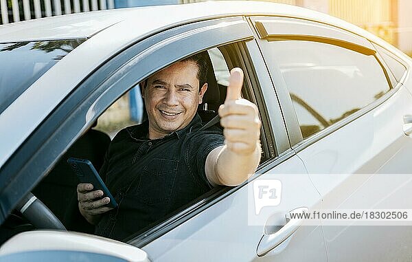 Lächelnd Fahrer hält Handy zeigt Daumen nach oben. Fahrer Mann zeigt Daumen nach oben  während Handy halten. Glücklicher Fahrer gibt einen Daumen nach oben auf der Straße. sicheres Fahren Konzept