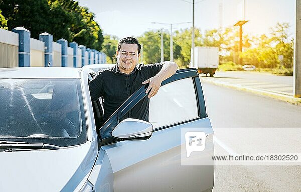 Smiling driver leaning on the car door. happy driver leaning on the car door in the street  Smiling owner with new car. Young latin man leaning on car door in the street