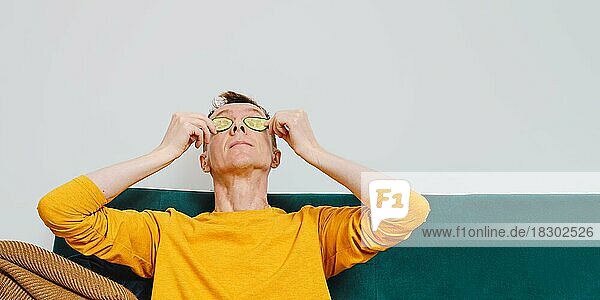 Älterer Mann entspannt auf Sofa mit Gurkenscheibe auf Augen
