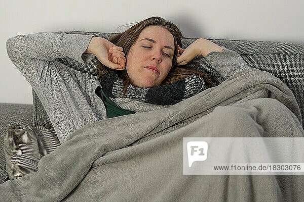 Frau  die von einem Nickerchen auf der Couch zu Hause aufwacht  bedeckt mit einer Decke und einem Schal