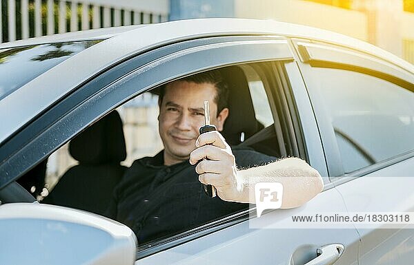 Happy man showing his new car keys  Person in his vehicle showing his car keys  Satisfied car buyer concept  Driver in his car showing the keys out the window