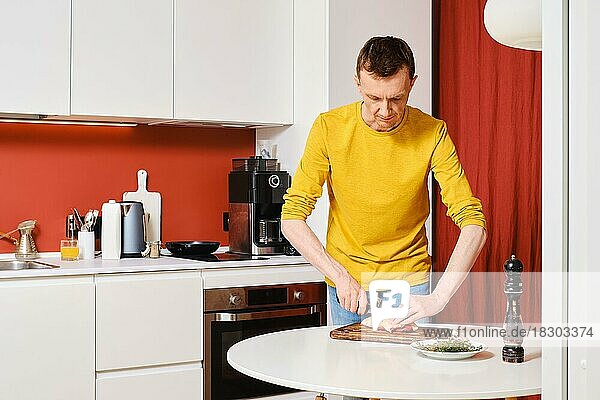 Ein Mann mittleren Alters schneidet in der Küche die Haut einer Entenbrust kreuzweise auf