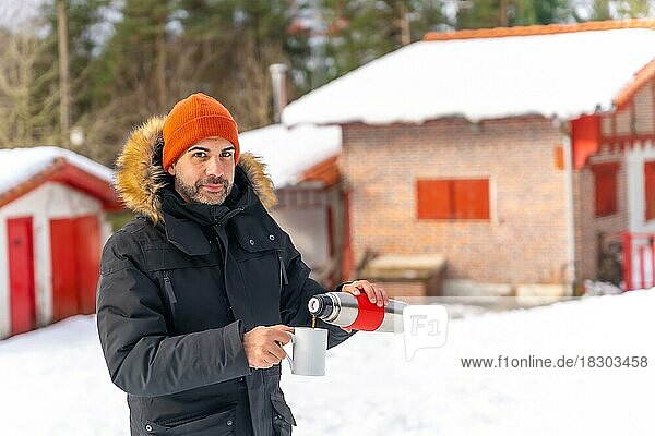 Mann trinkt im Winter im Schnee Kaffee aus einer heißen Thermoskanne