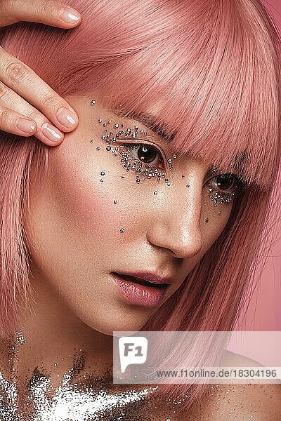 Schöne Frau in einer rosa Perücke und kreativem Make-up mit Strasssteinen. Schönes Gesicht. Foto im Studio aufgenommen