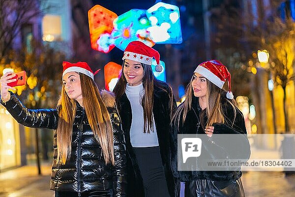 Christmas in the city at night  decoration in winter. Portrait of friends walking down the street taking a selfie  lifestyle