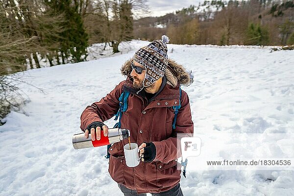 Mann trinkt im Winter im Schnee Kaffee aus einer heißen Thermoskanne  bevor er zum Trekking aufbricht