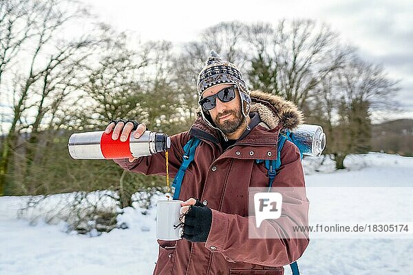Portrait of man having breakfast a hot coffee from a thermos in winter in the snow before starting the trekking