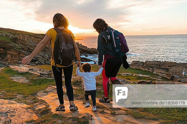 Lgbt Paar von Frauen mit einem Kind zu Fuß in den Sonnenuntergang an der Küste am Meer  Familie Lebensstil