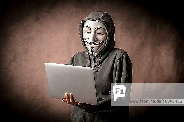 Mann mit anonymer Maske mit Sweatshirt und mit einem Laptop  Studioaufnahme