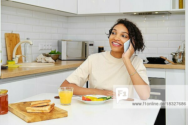 Glückliche attraktive afroamerikanische Frau  die während eines Telefonats beim Frühstück gute Nachrichten erhält