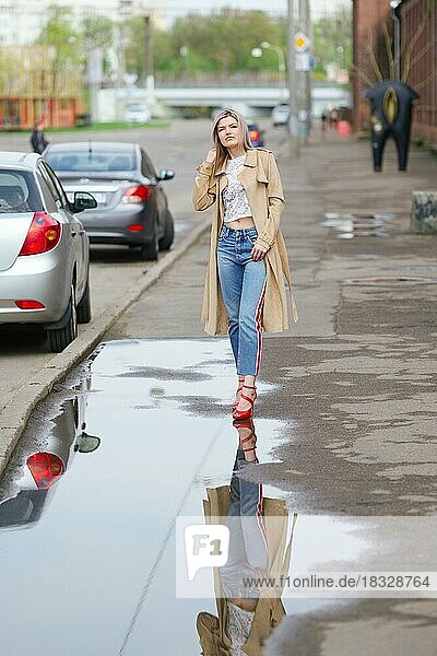Pretty girl in short jeans and raincoat walking on the street after the rain