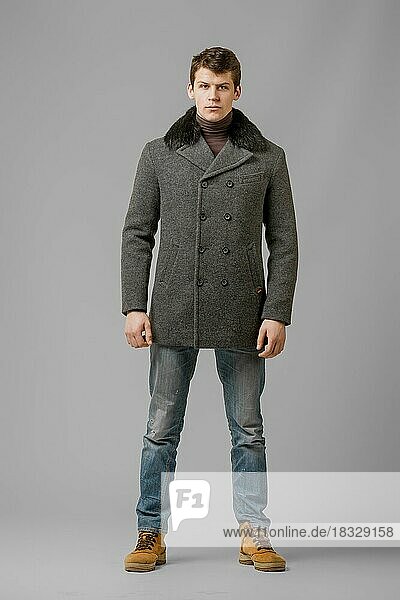 Ganzkörperporträt eines gut aussehenden Mannes in einem warmen Wintermantel  der im Studio posiert