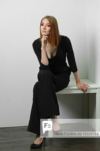 Elegantes junges Modemodell in schwarzem Overall mit tiefem Dekolleté posiert. Rote Haare  Abend-Make-up