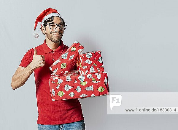 Weihnachten Mann hält Geschenk-Boxen und lächelnd mit Daumen nach oben. Lächelnder Mann in Weihnachtsmütze hält Weihnachtsgeschenk-Boxen geben Daumen nach oben. Freundlicher Mann in weihnachtlicher Kleidung hält Geschenkboxen