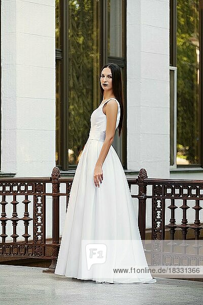Schönes Mädchen in langem weißen Kleid mit tiefem Ausschnitt. Fashion Model posiert auf der Terrasse eines Palastes